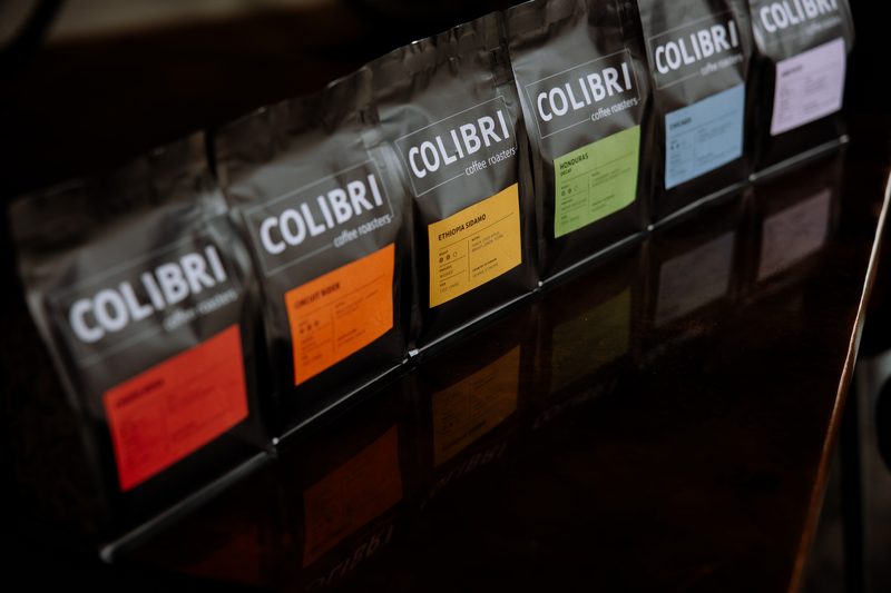 All six Colibri roasts in a row, shot at an angle so the labels run red, orange, yellow, green, blue, lavender
