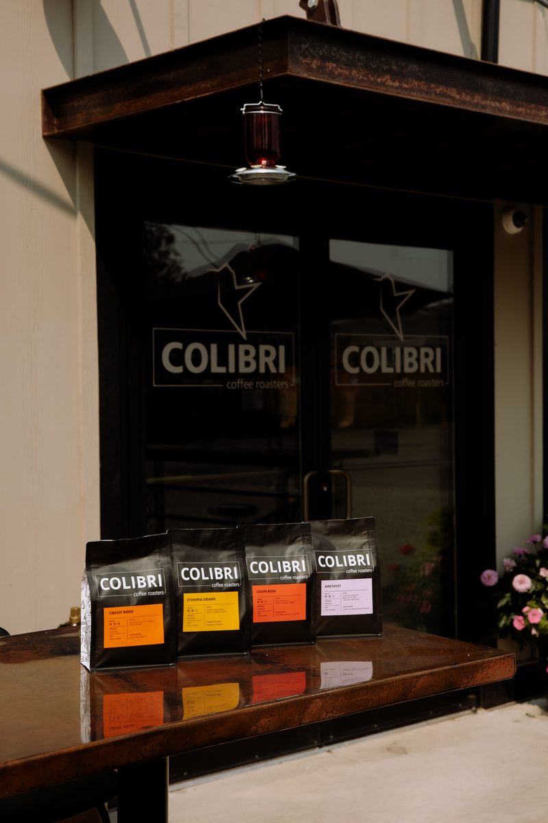 Four bags lined up on the patio table in front of the café's glass doors, under the hummingbird feeder
