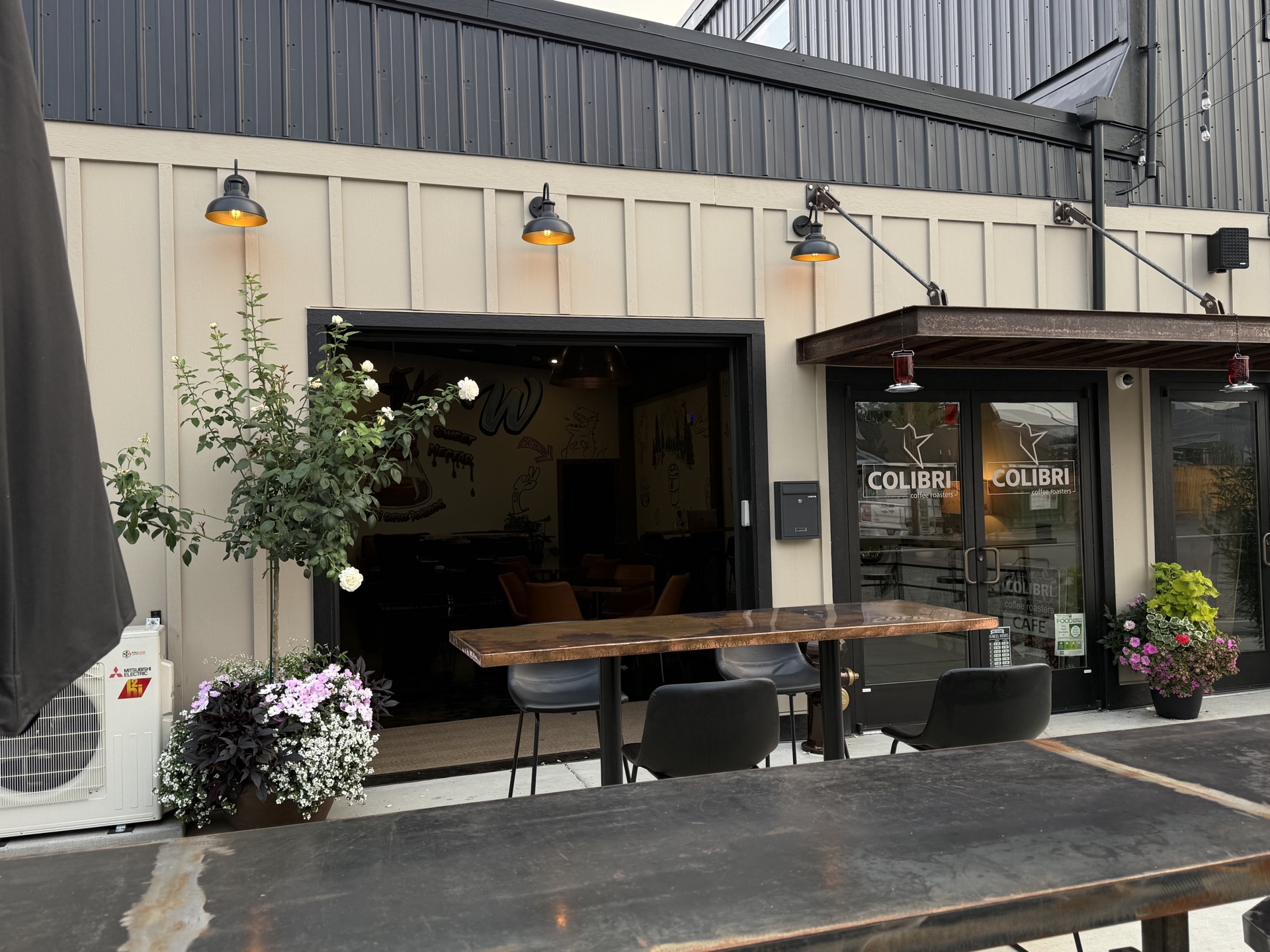 The Colibri storefront — double glass doors with white hummingbird decals under the rusted-copper awning, copper patio tables out front