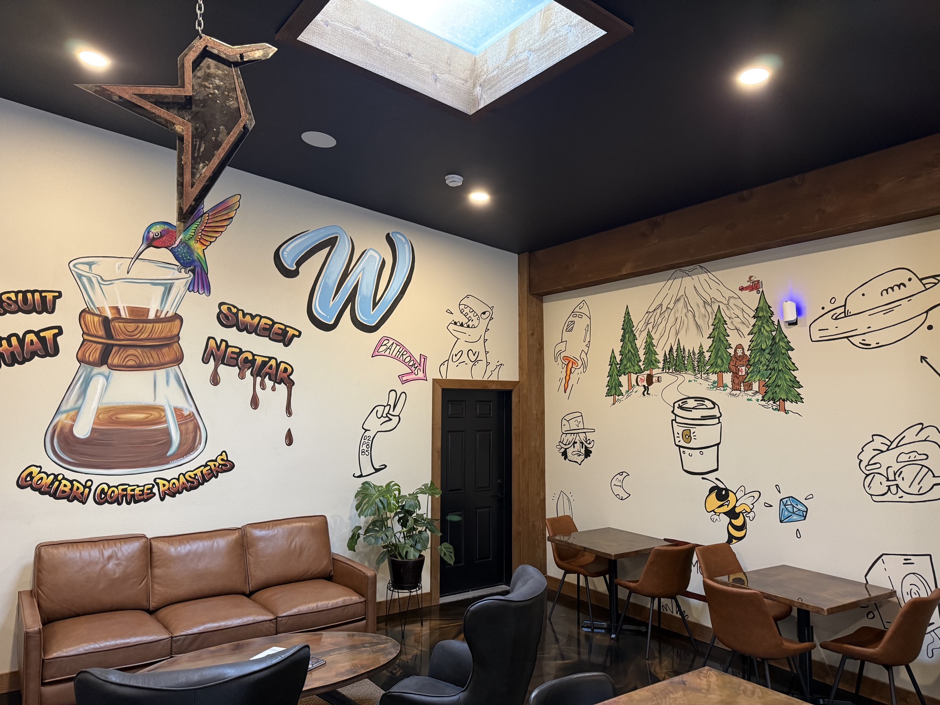 The Sweet Nectar mural — a hand-painted Chemex with a rainbow hummingbird drinking from it, above the cognac leather couch
